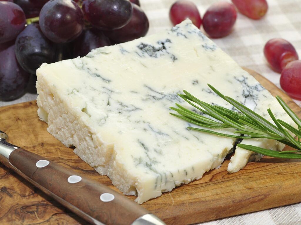 Käsestück mit Trauben und Schnittlauch auf Holzbrett